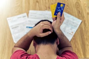 an aerial view of a stressed out man holding credit cards next to a table of bills